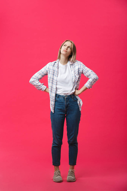 Thoughtful frowning young woman standing and thinking over pink background - Фото, изображение