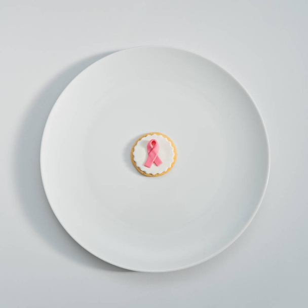 Ciasteczka z różową wstążką, jako znak walki z rakiem piersi na talerzu biały na białym tle. Abstrakcyjne pojęcie International raka dnia 4 lutego, płaskie świeckich kartkę z życzeniami, format kwadratowy - Zdjęcie, obraz