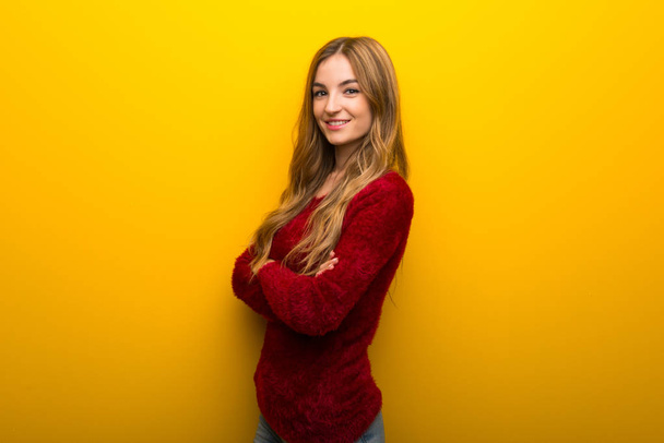 Mladá dívka na pulzující žluté pozadí vedení zkříženými zbraní v boční poloze a s úsměvem - Fotografie, Obrázek