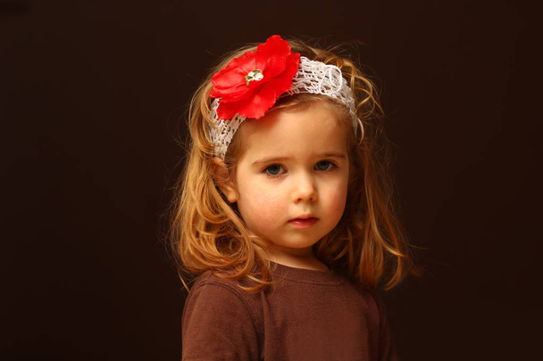 Porträt eines niedlichen zweijährigen Kleinkindes mit rotem Blumenstirnband, isoliert auf schwarz - Foto, Bild