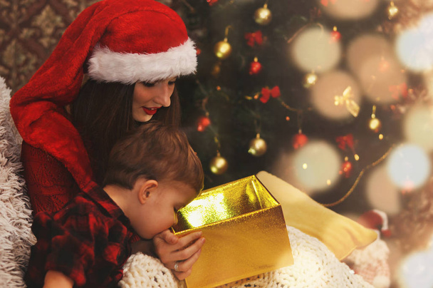 Молодая красивая мать со своим маленьким сыном смотрят в волшебную светящуюся коробку с подарком
. - Фото, изображение