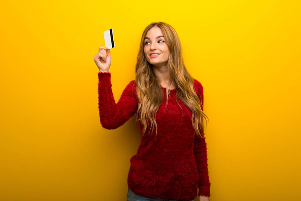 Fiatal lány élénk sárga háttér gazdaság egy hitelkártya, és a gondolkodás - Fotó, kép