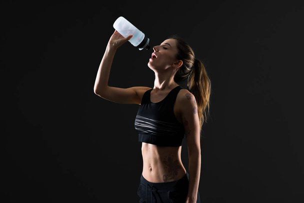 Sport woman with a bottle of water on dark background - Photo, Image