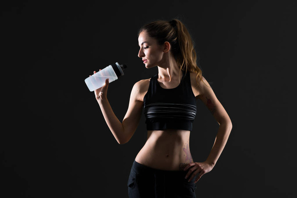 Sport woman with a bottle of water on dark background - Foto, afbeelding