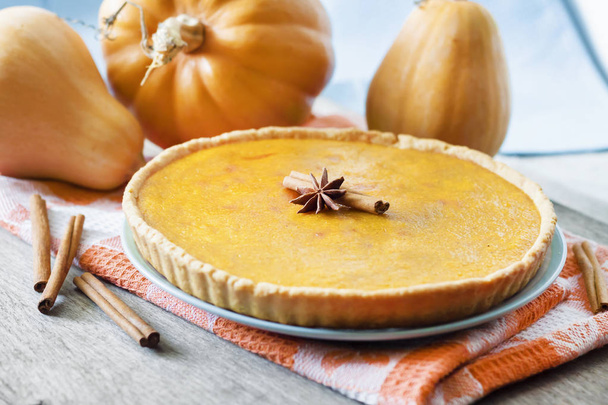 Homemade spicy pumpkin pie with cinnamon on a table with pumpkings at background - Foto, imagen