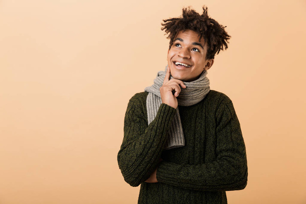 Portrait of joyful african american man wearing sweater and looking upward isolated over beige background - Foto, immagini