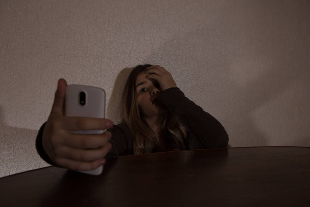 Одномісний сумний підліток тримає мобільний телефон плаче на ліжку в її спальні з темним світлом
 - Фото, зображення