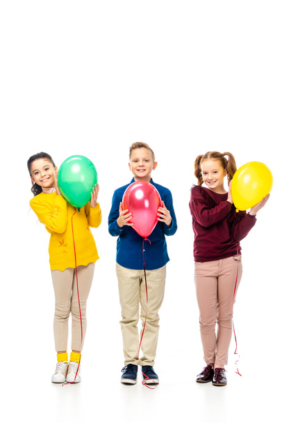 cute boy and schoolgirls smiling, holding multicolored balloons and looking at camera isolated on white - Valokuva, kuva