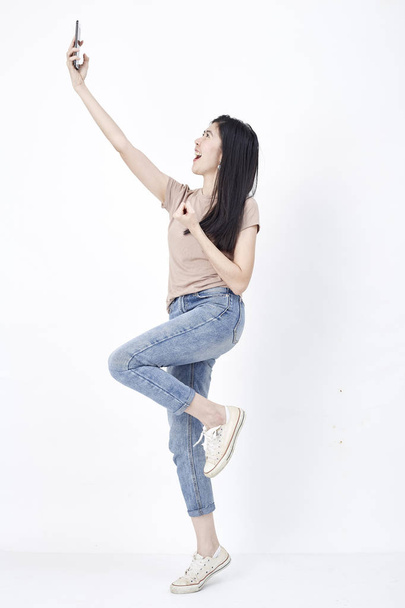 Close up full length size body photo of jump pretty charming she her her girl hand holding phone skype online internet in flight showing wear casual clothes white background
 - Foto, imagen