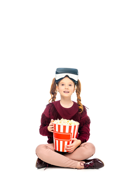 παιδί με σετ κεφαλής εικονικής πραγματικότητας στο κεφάλι κρατώντας κουβά ριγέ ποπ κορν που απομονώνονται σε λευκό - Φωτογραφία, εικόνα