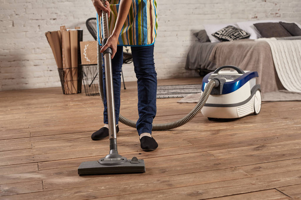 Faceless middle section of young woman using vacuum cleaner in home living room floor, doing cleaning duties and chores, meticulous interior. - Photo, Image
