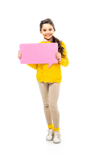 happy schoolgirl in yellow sweater holding pink speech bubble and looking at camera isolated on white - Фото, изображение