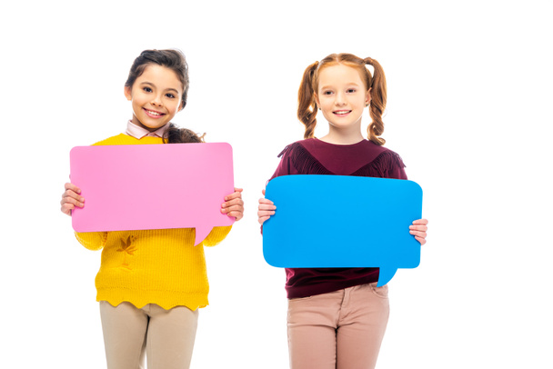 smiling schoolgirls holding multicolored speech bubbles and looking at camera isolated on white - Fotó, kép