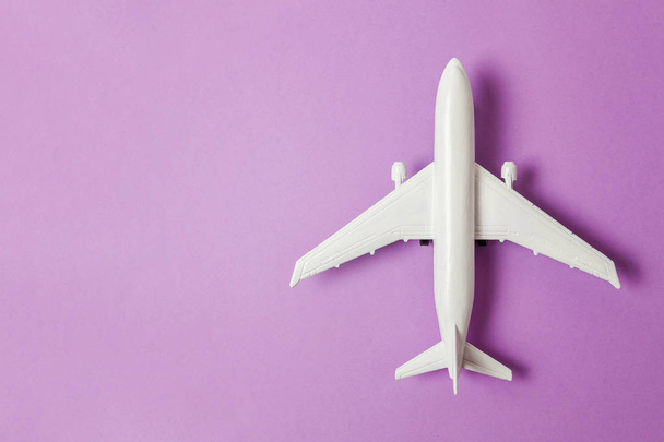 Simply flat lay design miniature toy model plane on violet purple pastel colorful paper trendy background. Travel by plane vacation summer weekend sea adventure trip journey ticket tour concept - 写真・画像