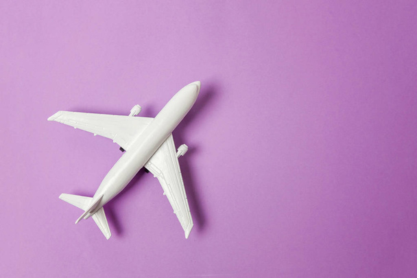 Gewoon plat lag ontwerp miniatuur speelgoed model vliegtuig op violet paars pastel kleurrijke papier trendy achtergrond. Reizen per vliegtuig vakantie zomer weekend zee avontuur reis reis ticket tour concept - Foto, afbeelding