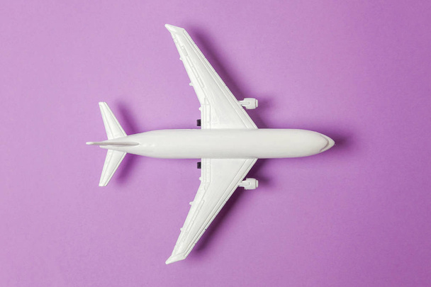 Po prostu płaski świeckich projekt miniaturowych zabawka modelu samolotu na tle modny fioletowy fioletowy kolorowy papier pastel. Podróż przez samolot wakacje lato weekend morze przygody podróży podróż bilet tour koncepcja - Zdjęcie, obraz