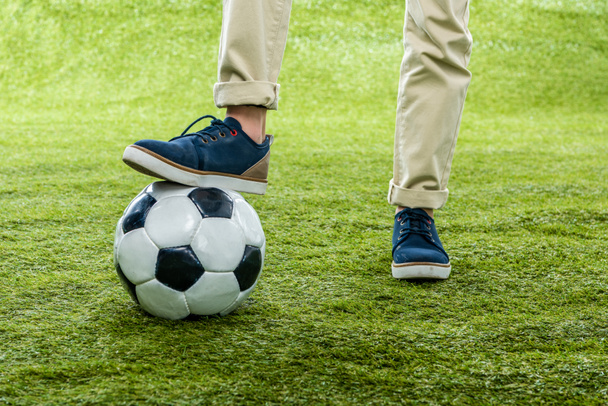 cropped view of boy with leg standing on soccer ball on lawn - Foto, afbeelding