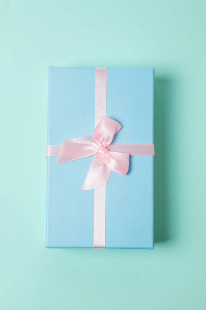 Pequeña caja de regalo envuelta en papel azul aislado sobre fondo geométrico de moda colorido pastel rosa. Navidad Año Nuevo cumpleaños celebración de San Valentín presente concepto romántico
 - Foto, Imagen