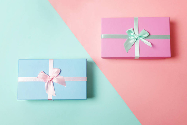 Small gift box wrapped pink and blue paper isolated on blue and pink pastel colorful trendy geometric background. Christmas New Year birthday valentine celebration present romantic concept - Photo, Image