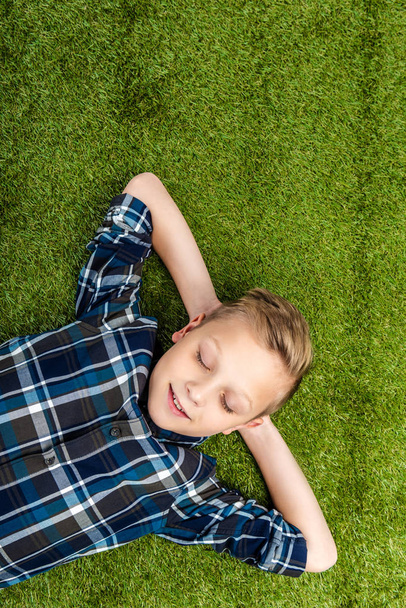 top view of cute boy lying on lawn with closed eyes - Photo, image