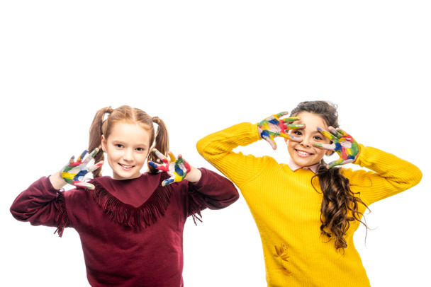 cheerful schoolgirls smiling, showing hands painted in colorful paints and looking at camera isolated on white - Foto, Imagen