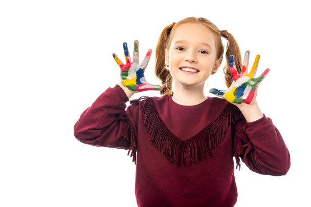 glimlachend schoolmeisje camera kijken en handen tonen geschilderd in kleurrijke verf geïsoleerd op wit - Foto, afbeelding