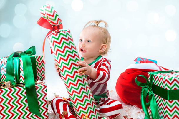 Cute baby girl 1 year old near santa hat posing over Christmas background. Sitting on floor with Christmas ball. Holiday season. - Foto, Imagem