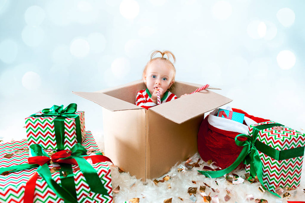 Cute baby girl 1 year old sitting at box over Christmas background. Holiday season. - Photo, image