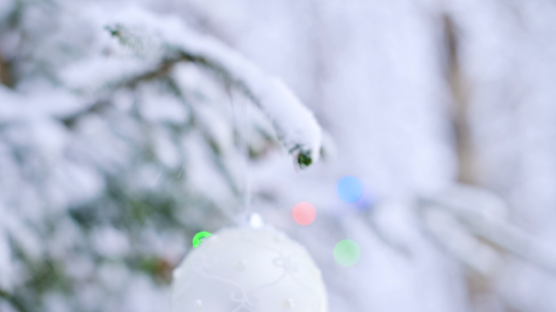 Close-up de um brinquedo de Natal em uma árvore animada coberta de neve na floresta de inverno no fundo das luzes. DOF pequeno
 - Filmagem, Vídeo