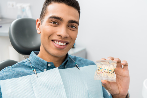 bonito afro-americano homem segurando modelo de mandíbula dental com aparelho
 - Foto, Imagem