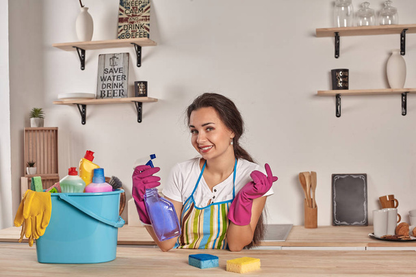 mooie vrolijke brunette vrouw in handschoenen schoonmaak moderne keuken - Foto, afbeelding