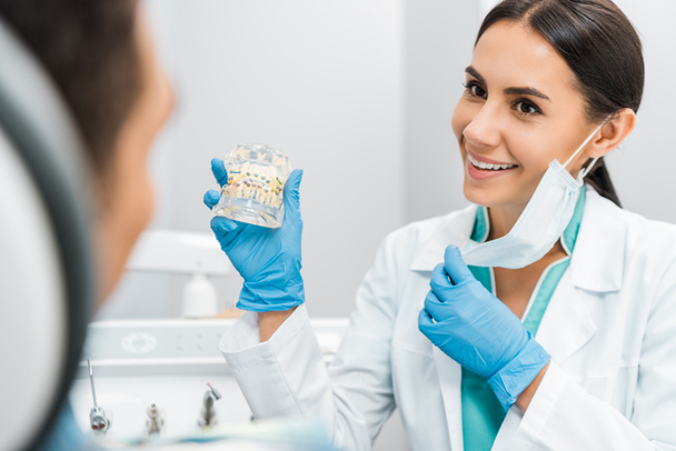 smiling female stomatologist showing dental jaw model with braces to patient  - Fotó, kép