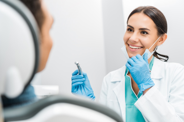 Lächelnde Stomatologin hält Bohrer in der Nähe von Patientin  - Foto, Bild