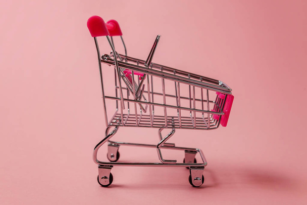 Petit supermarché épicerie poussette chariot pour jouet shopping avec des roues isolées sur fond rose pastel papier coloré à la mode. Vente acheter centre commercial magasin concept de consommation. Espace de copie
 - Photo, image