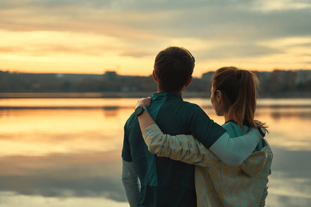 Visão traseira, corredores casal sonhando enquanto olha para o nascer do sol no lago. feliz romântico ajuste jovem casal desfrutando por do sol
 - Foto, Imagem