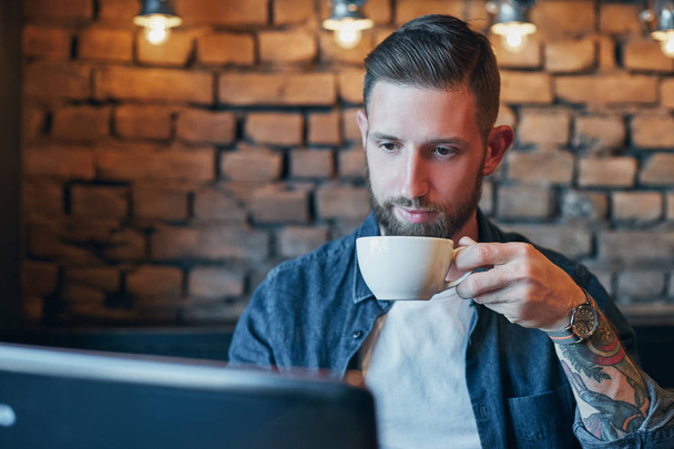 Νεαρός άνδρας πίνοντας καφέ σε καφετέρια της πόλης κατά τη διάρκεια του γεύματος και να εργάζονται στο lap-top - Φωτογραφία, εικόνα