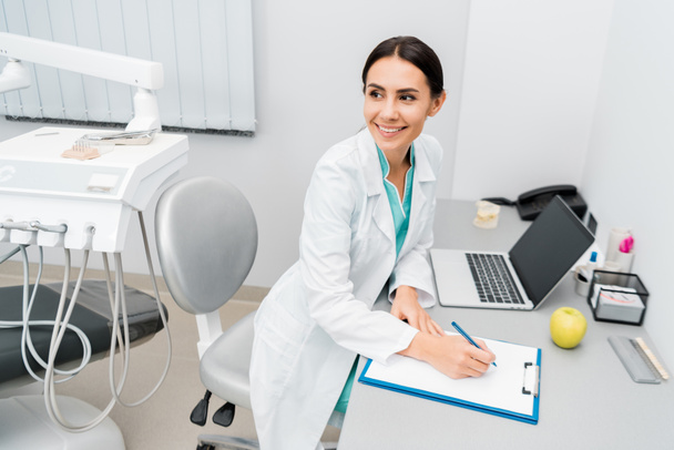 attractive female doctor making notes near laptop  - Photo, image