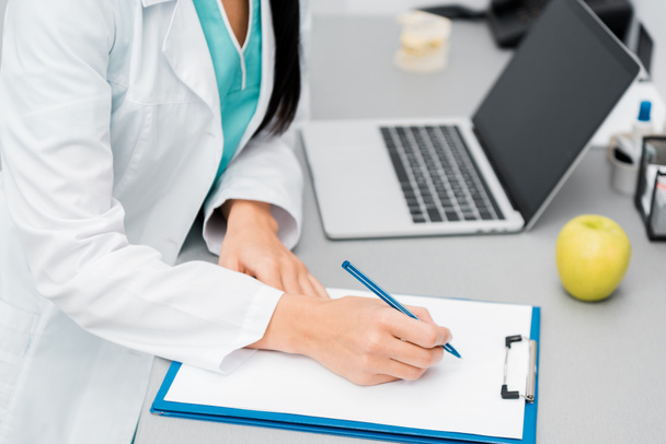 vista cortada de médico fêmea fazendo anotações perto do laptop
  - Foto, Imagem