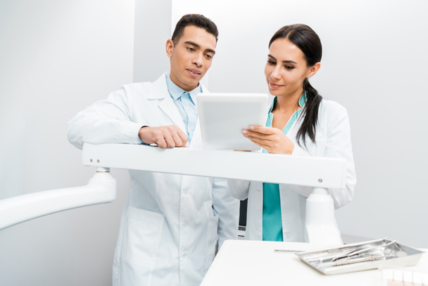 Multikulti-Ärzte stehen im weißen Kittel und schauen auf digitales Tablet  - Foto, Bild