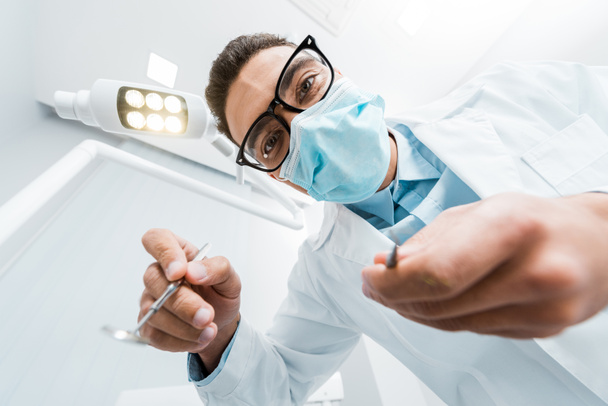 стоматологические инструменты в руках мужчины-стоматолога в очках и маске
 - Фото, изображение