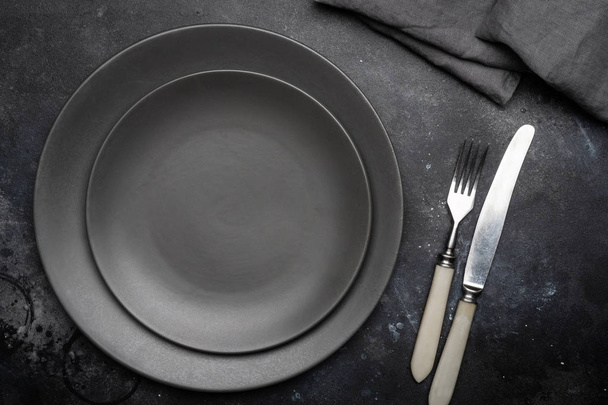 Пустая серая тарелка (керамическая) на темно-сером фоне с ножом и вилкой, украшенная букетом лаванды и салфеткой. Серая минималистическая концепция. Копирование пространства
. - Фото, изображение