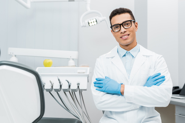 guapo afroamericano dentista en gafas de pie con los brazos cruzados
  - Foto, Imagen