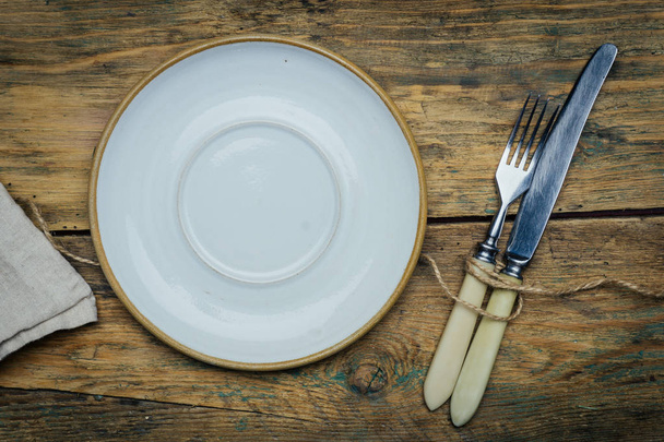 Пустая белая деревенская тарелка на старом деревянном фоне с ножом, вилкой и салфеткой. Концепция сельской пищи. Копирование пространства
 - Фото, изображение