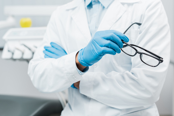 Ausgeschnittene Ansicht eines Arztes, der mit verschränkten Armen steht und eine Brille hält  - Foto, Bild