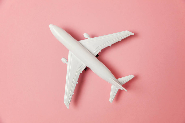 Simply flat lay design miniature toy model plane on pink pastel colorful paper trendy background. Travel by plane vacation summer weekend sea adventure trip journey ticket tour concept - Photo, Image
