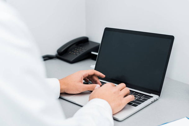 selective focus of male hands of african american doctor typing on laptop with blank screen  - Foto, imagen