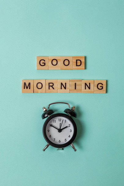 Simply flat lay design alarm clock and Inscription GOOD MORNING letters word on blue pastel colorful trendy background. Breakfast time. Good morning wake up awake concept. Top view copy space - Foto, afbeelding