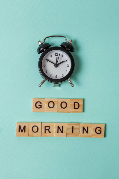 Simply flat lay design alarm clock and Inscription GOOD MORNING letters word on blue pastel colorful trendy background. Breakfast time. Good morning wake up awake concept. Top view copy space - Фото, зображення