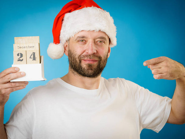 Man wearing santa claus christmas hat holding calendar with 24 december date, on blue - Photo, image