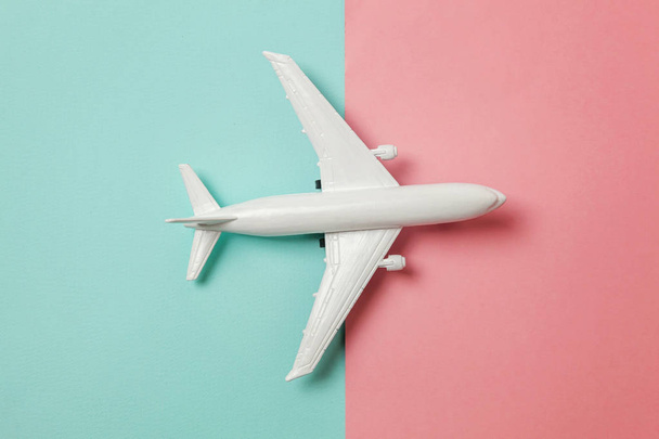 Simply flat lay design miniature toy model plane on blue and pink pastel colorful paper trendy geometric background. Travel by plane vacation summer weekend sea adventure trip concept - Photo, Image